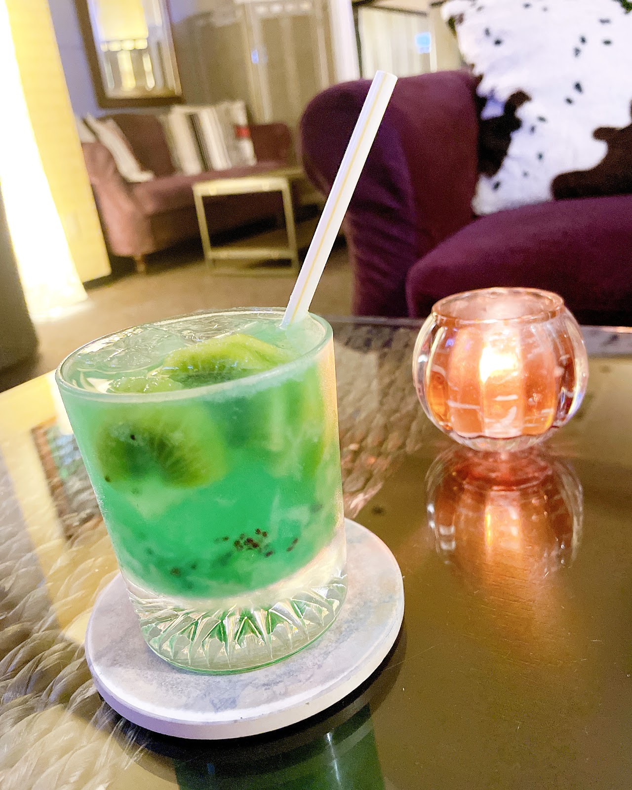 キウイの輪切りが入った緑色のドリンクとキャンドル。奥に紫のソファ。