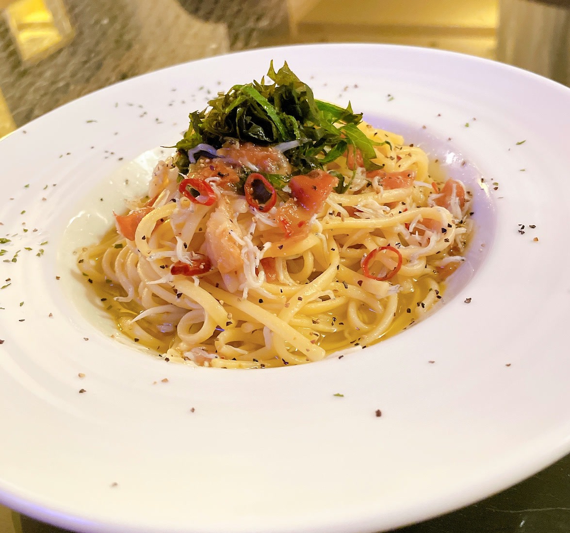 オリーブオイルのパスタに、しらすのような小魚、トマト、赤唐辛子の輪切り。上に細切りの青菜。